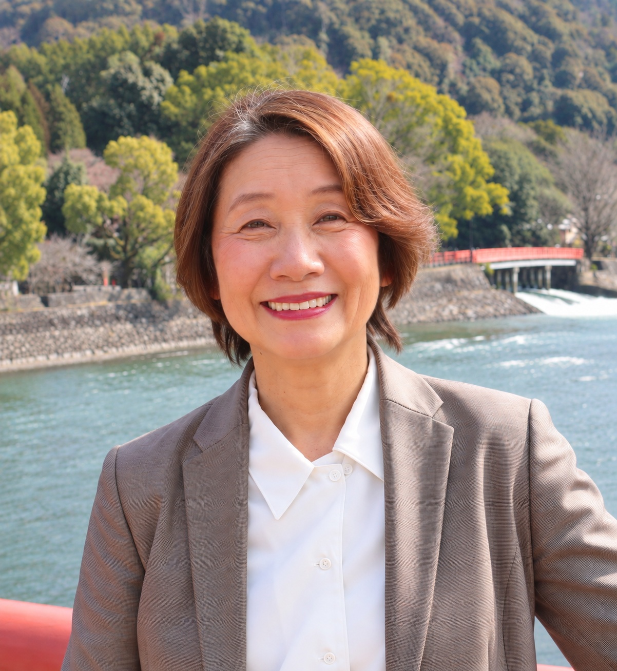 宇治の川辺で微笑むジャケット姿の佐々木まゆみ